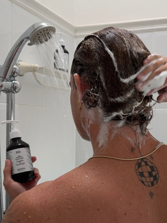 Person washing hair with a bottle of shampoo in a shower