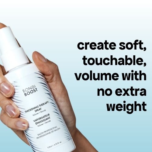 Hand holding a bottle of Bondi Boost Thickening Therapy Spray with text on a light blue background