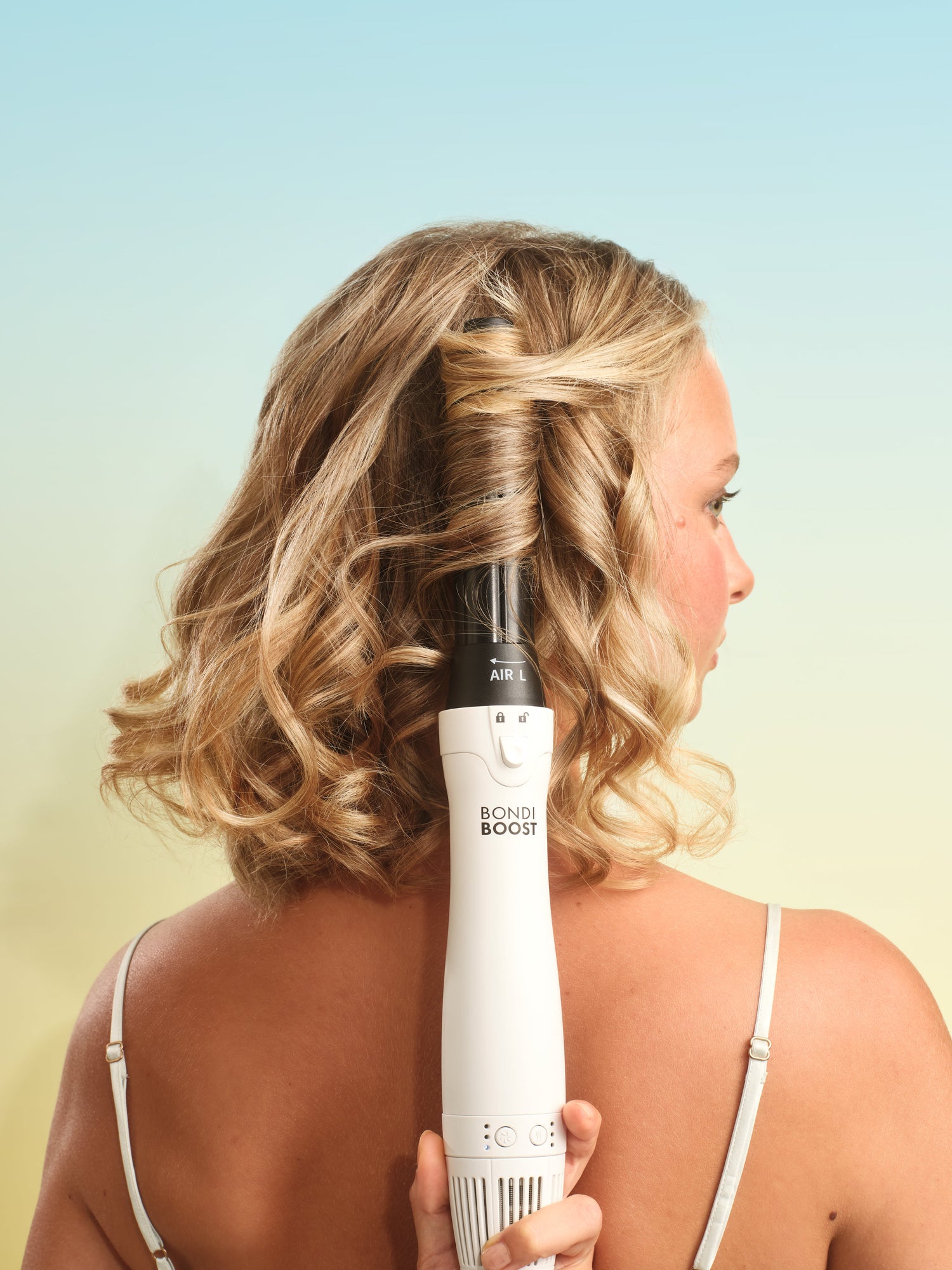 Woman using a hair styling tool on her hair with a gradient background